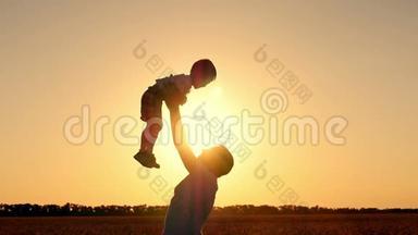 父亲在一个幸福家庭的夕阳剪影中把儿子扔到麦田里。